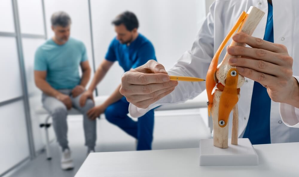 Medico ortopedico spiega la struttura dei legamenti del ginocchio con un modellino anatomico a un paziente